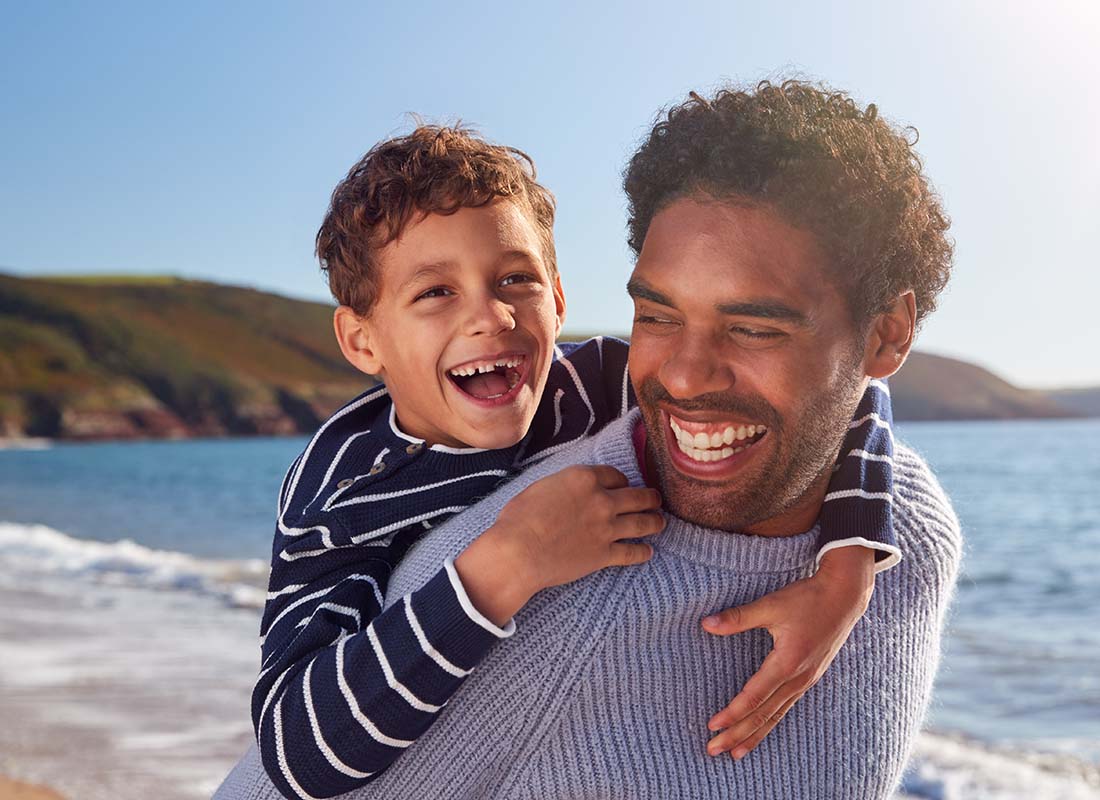 Excess Liability Insurance - Father and Son Laughing as Dad Gives Son a Piggyback Ride as They Walk along the Beach Together in the Winter